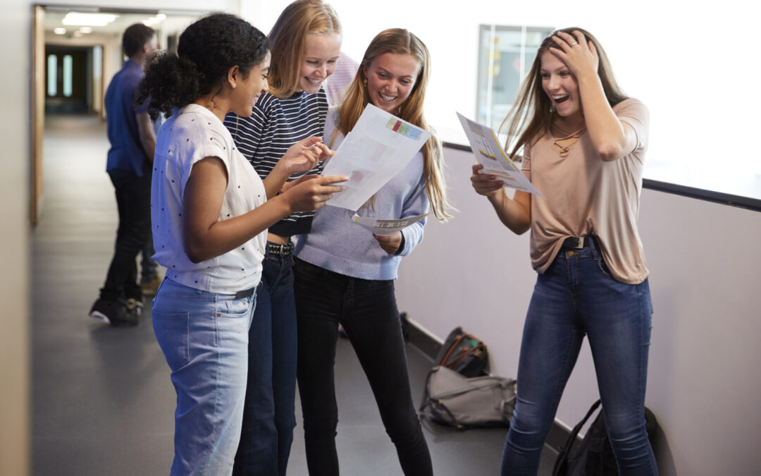 Excited Female Teenage High School Students Celebrating Exam Results In School Corridor